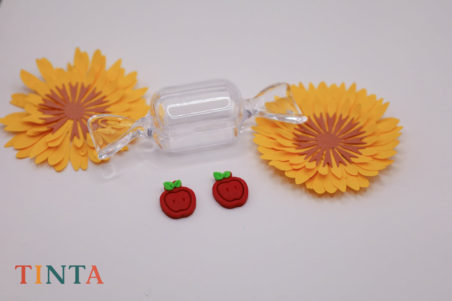 Clear candy with yellow sunflower-shaped ends on a white background, featuring the brand 'TINTA'.