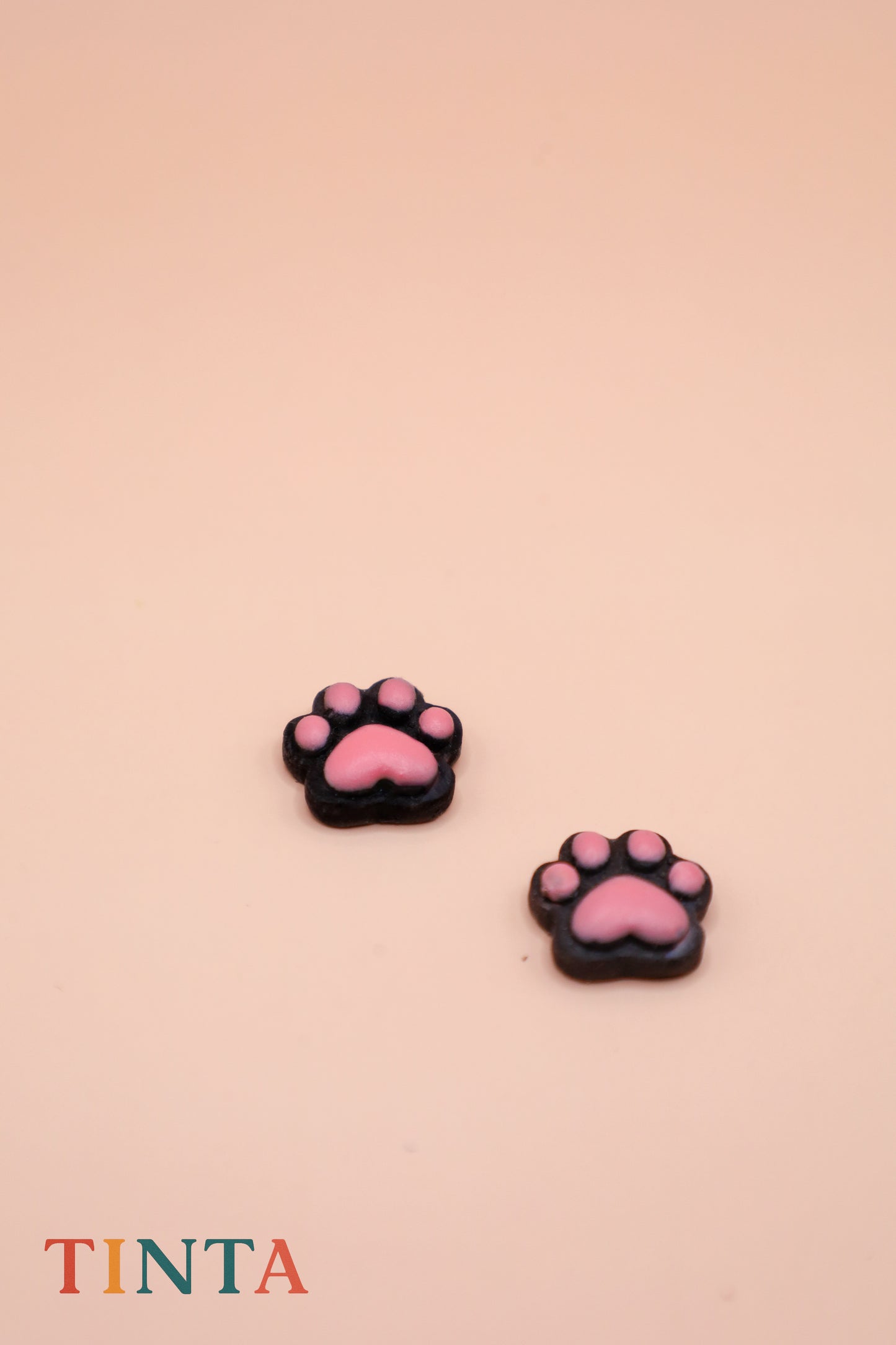 Pink paw-shaped earrings on a beige background with 'TINTA' branding.