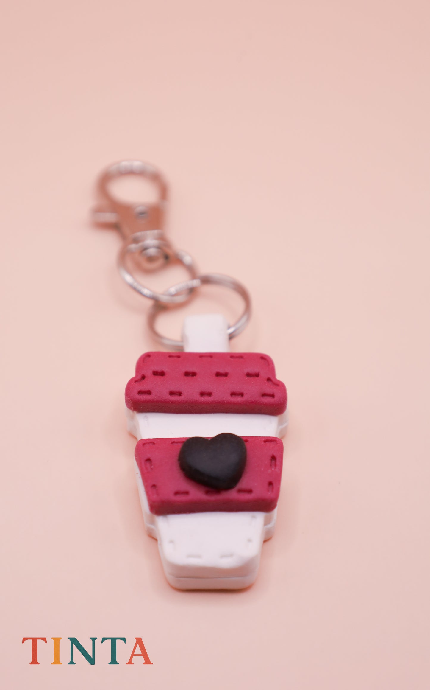 Keychain shaped like a coffee cup with a heart on a pink background, featuring the brand 'Tinta'.