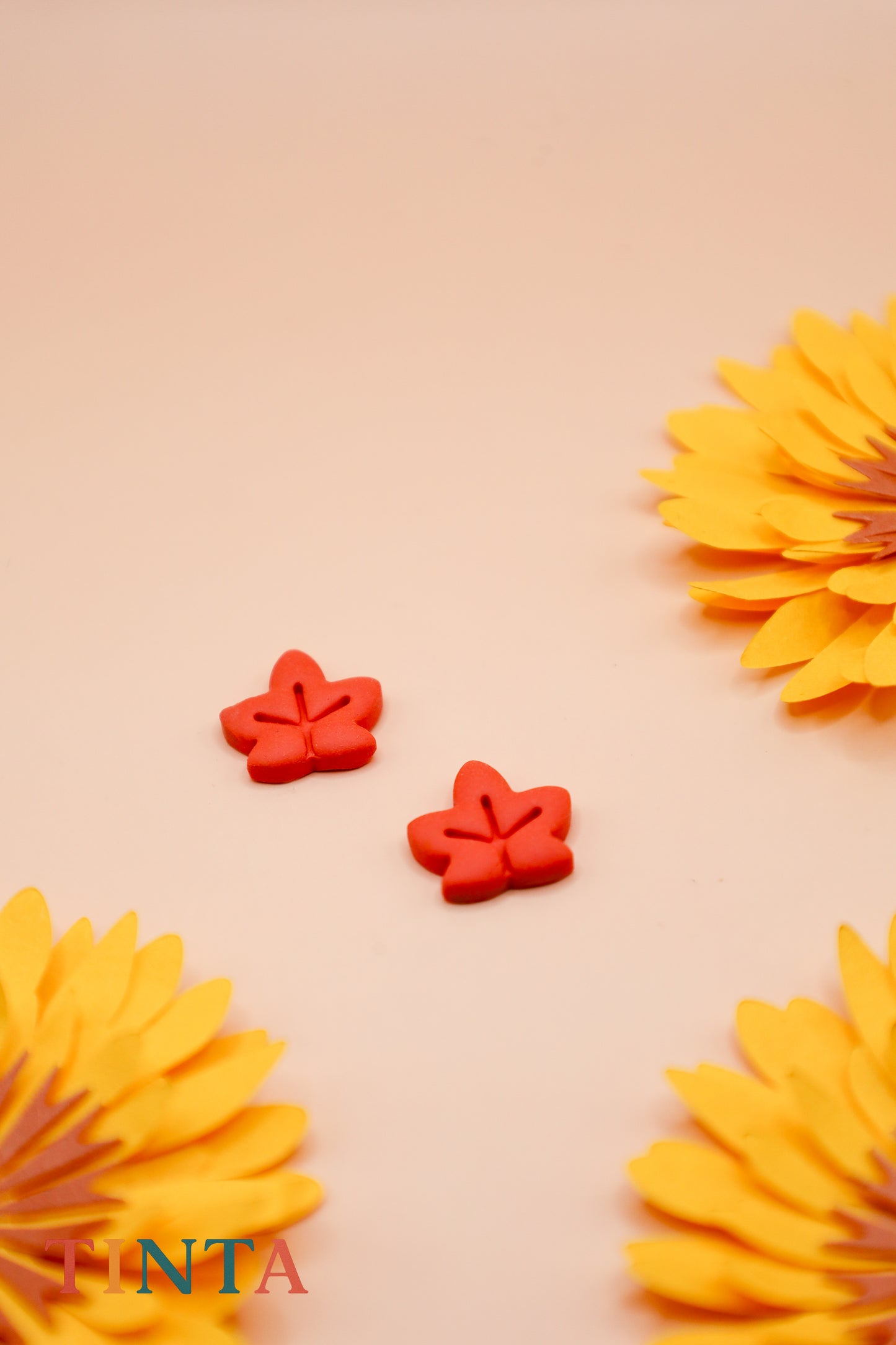 Maple leave earrings on a beige background with yellow flowers.