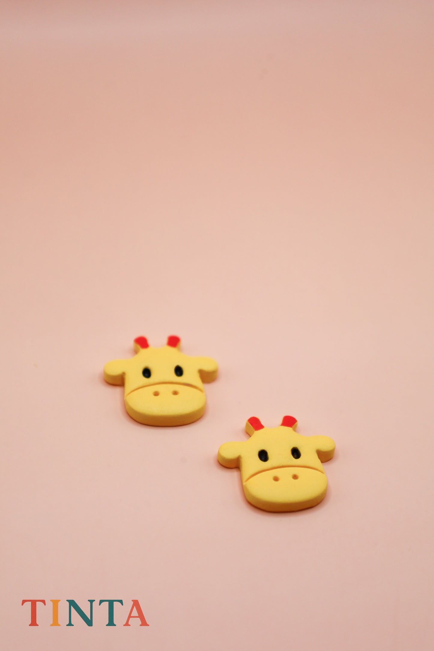 Two yellow giraffe-shaped objects on a pink background with 'TINTA' branding.