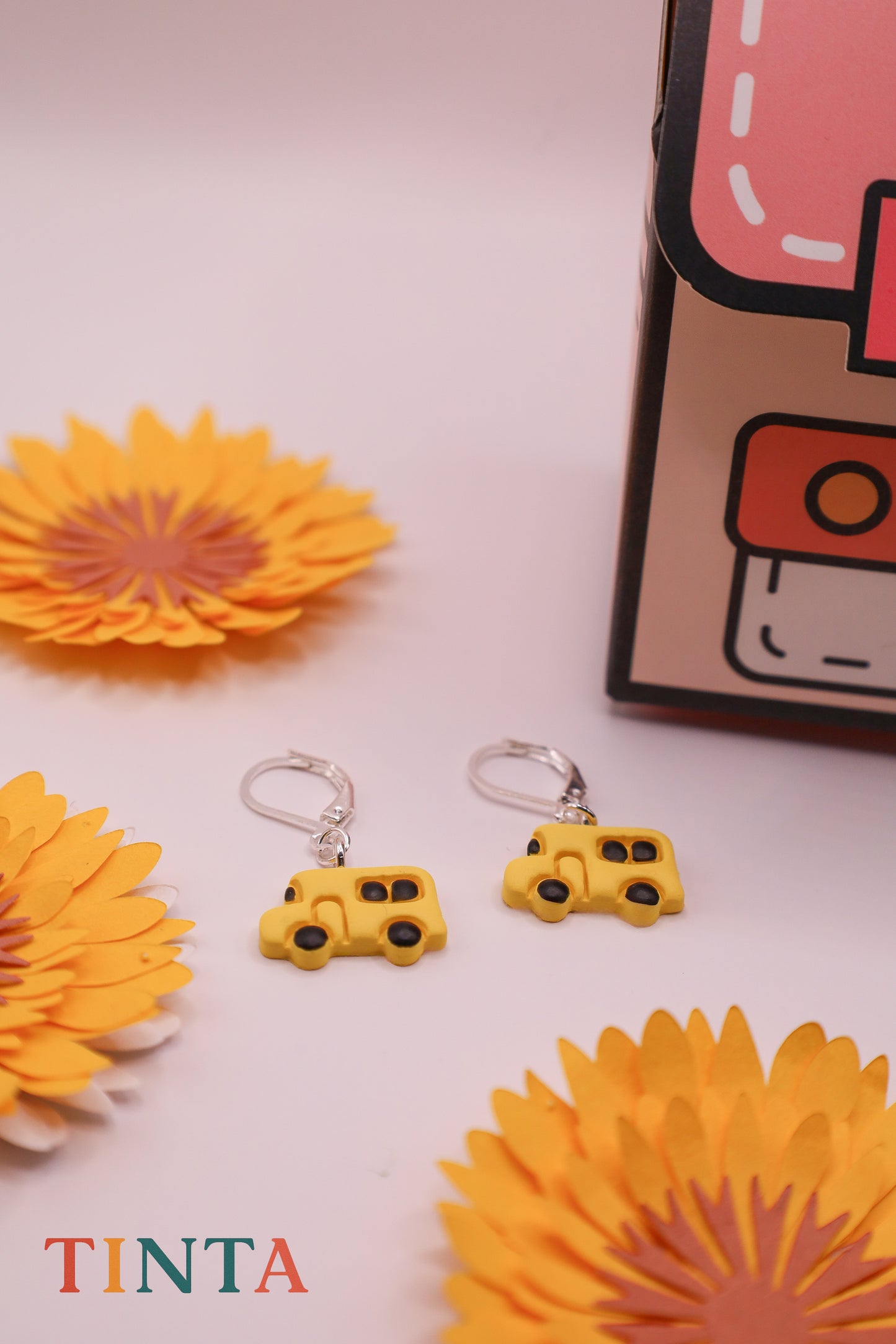 Yellow bus-shaped keychains with decorative flowers and a box in the background.