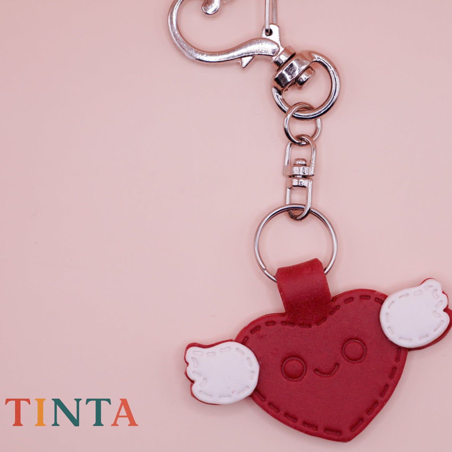 Heart-shaped keychain with a smiling face on a pink background, featuring the brand 'Tinta'.