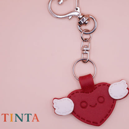 Heart-shaped keychain with a smiling face on a pink background, featuring the brand 'Tinta'.