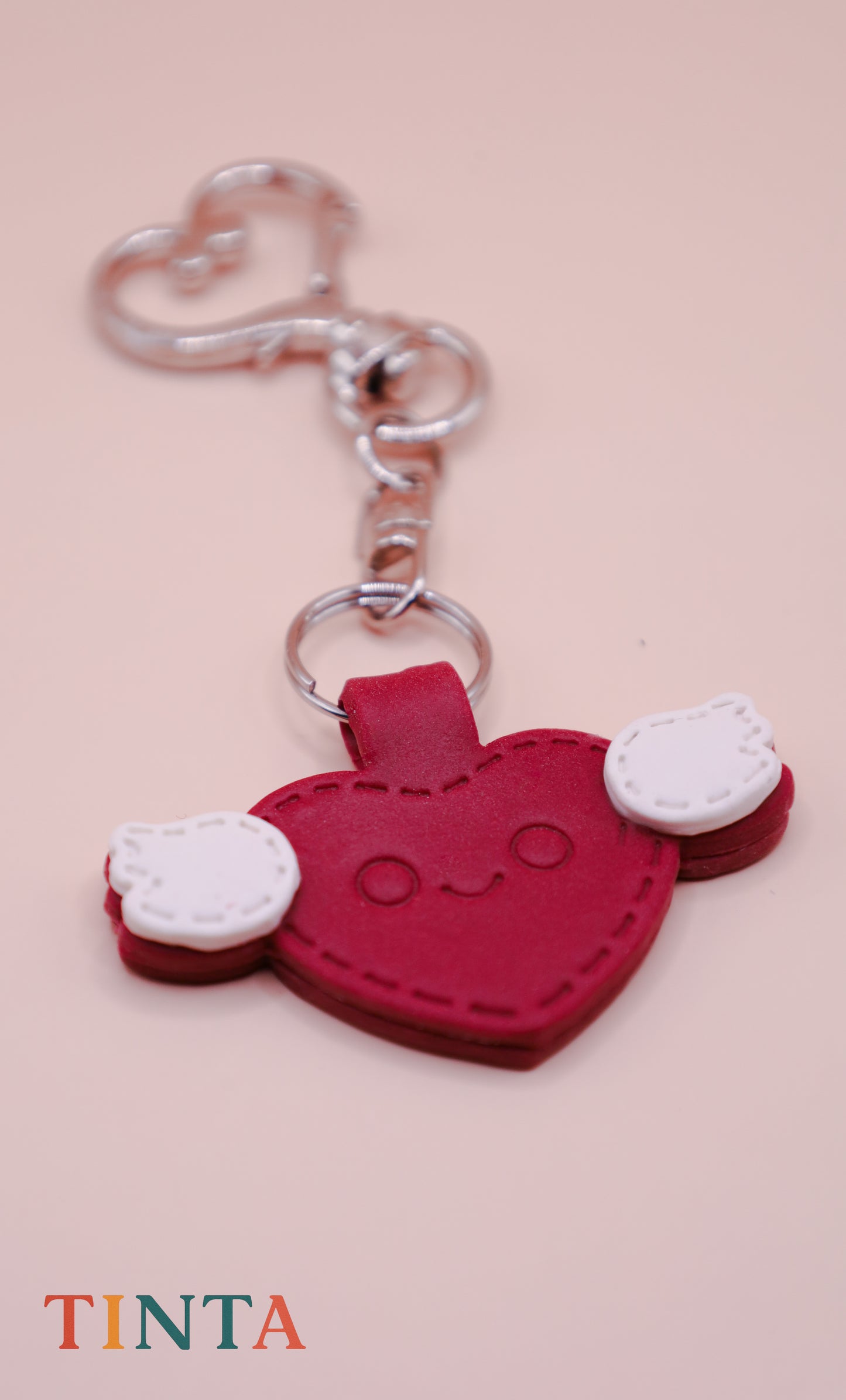 Red heart-shaped keychain with white accents on a pink background, featuring the brand 'Tinta'.
