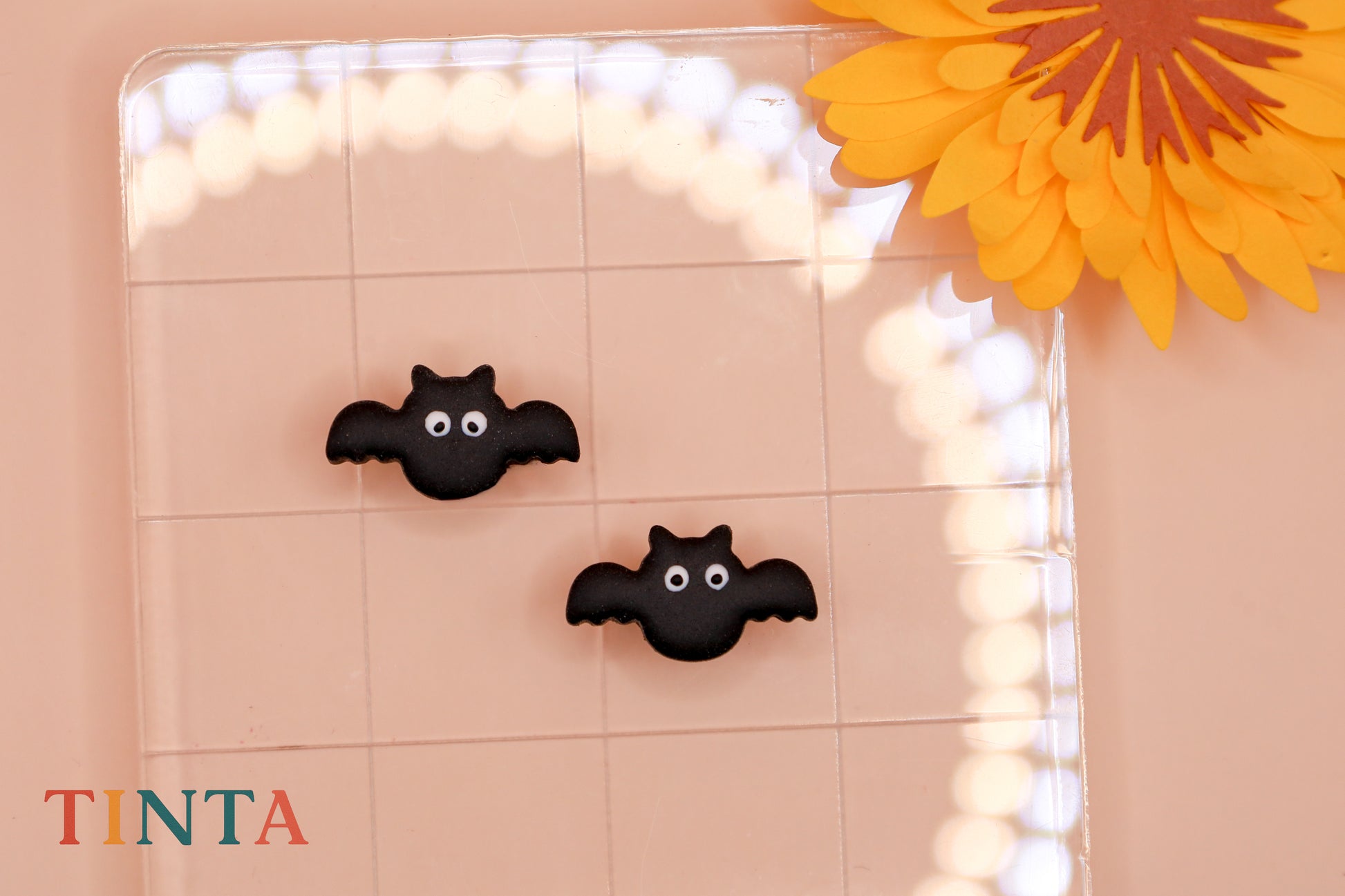 Black bat-shaped decorations on a tiled wall with a blurred light effect and a yellow flower.