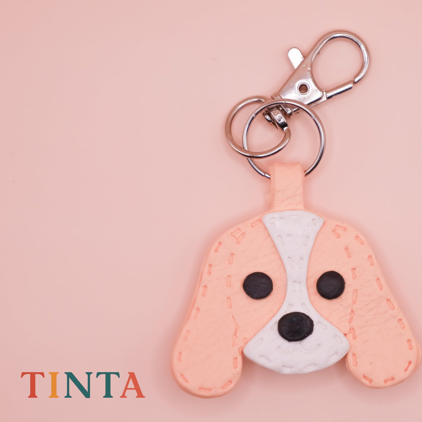 Dog-shaped keychain on a pink background with 'TINTA' branding.