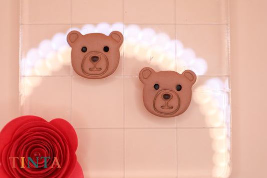Two teddy bear heads on a tiled wall with decorative lights and a red flower.