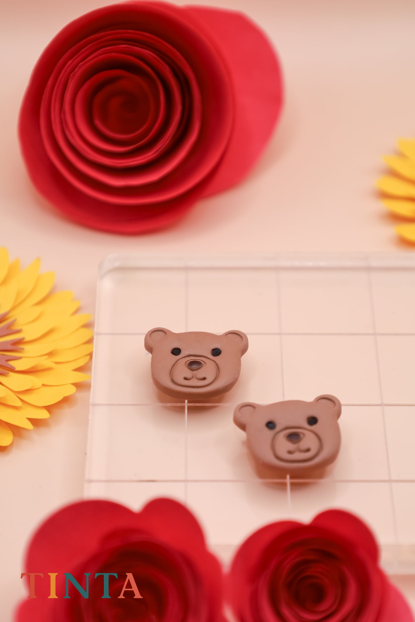 Two small brown bear-shaped objects on a tiled surface with red flowers and yellow leaves in the background.