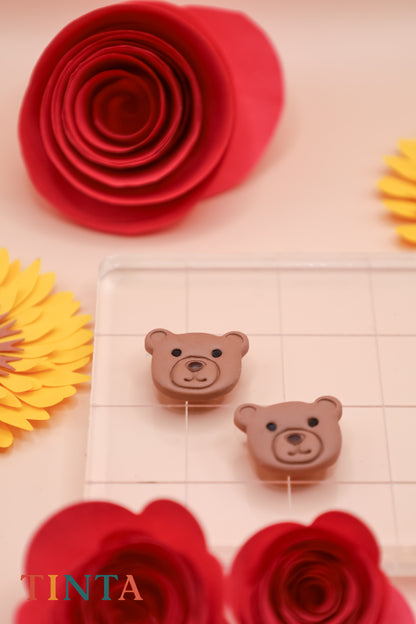 Two small brown bear-shaped objects on a tiled surface with red flowers and yellow leaves in the background.