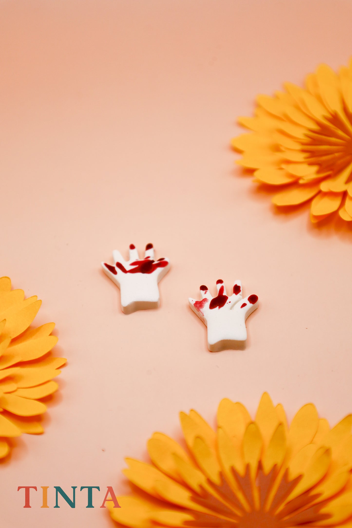 White crowns with red accents on a peach background with orange flowers, featuring the brand 'Tinta'.