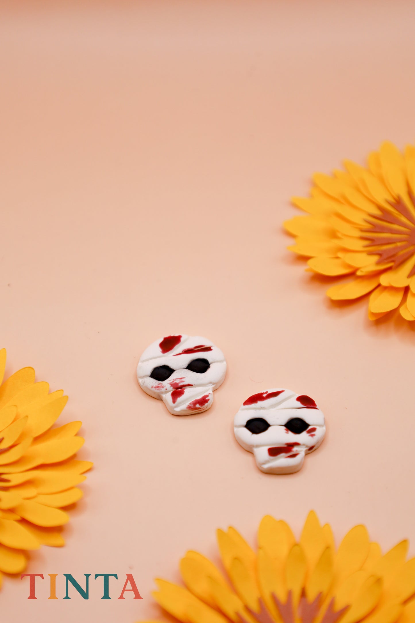 Two decorative skull-shaped cookies with red and white icing on a pink background with yellow flowers.