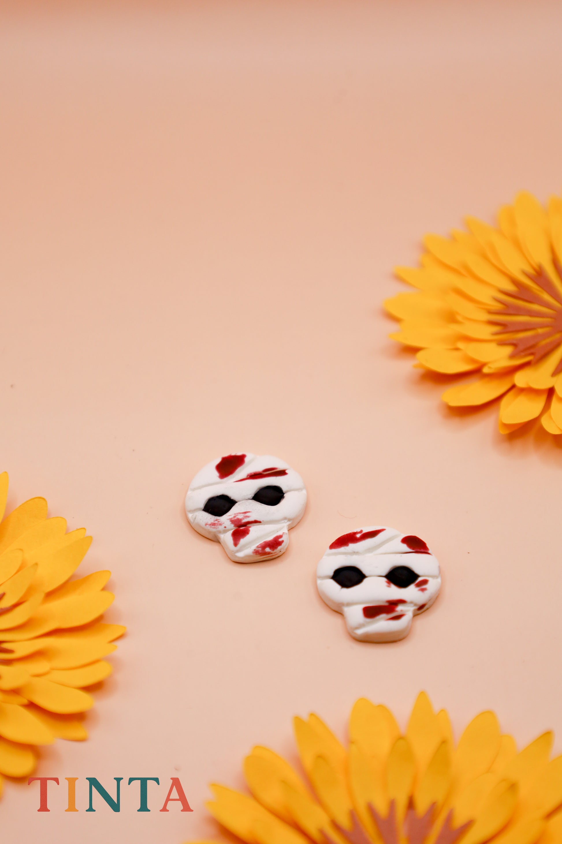 Two decorative skull-shaped cookies with red and white icing on a pink background with yellow flowers.
