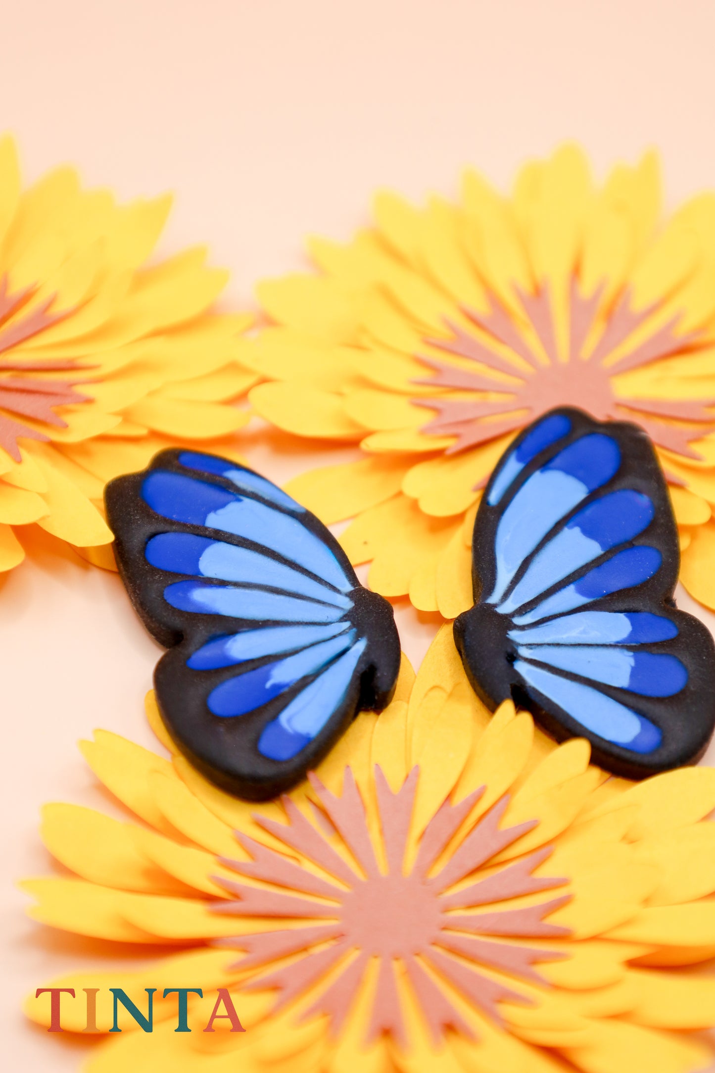 Blue butterfly-shaped objects on yellow flowers with 'TINTA' branding.