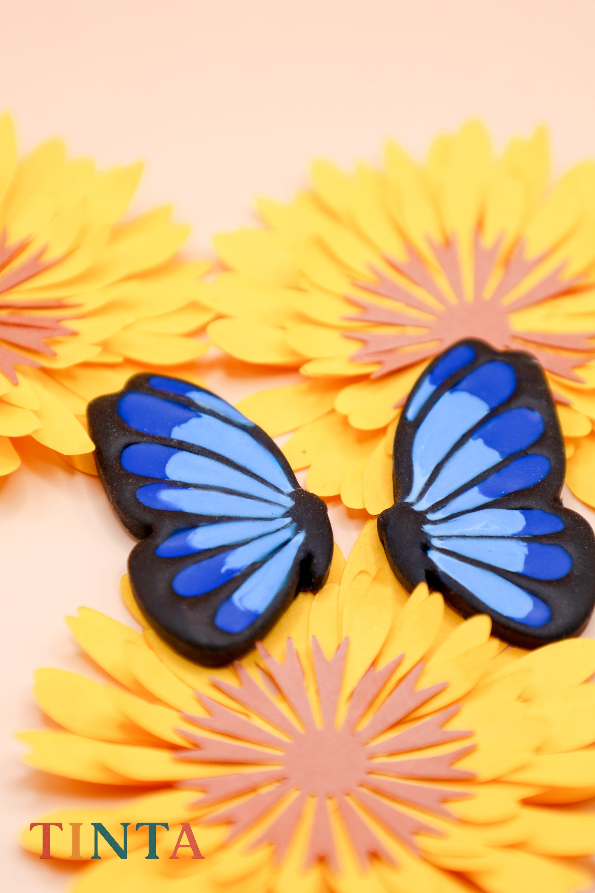 Blue butterfly-shaped objects on yellow flowers with 'TINTA' branding.