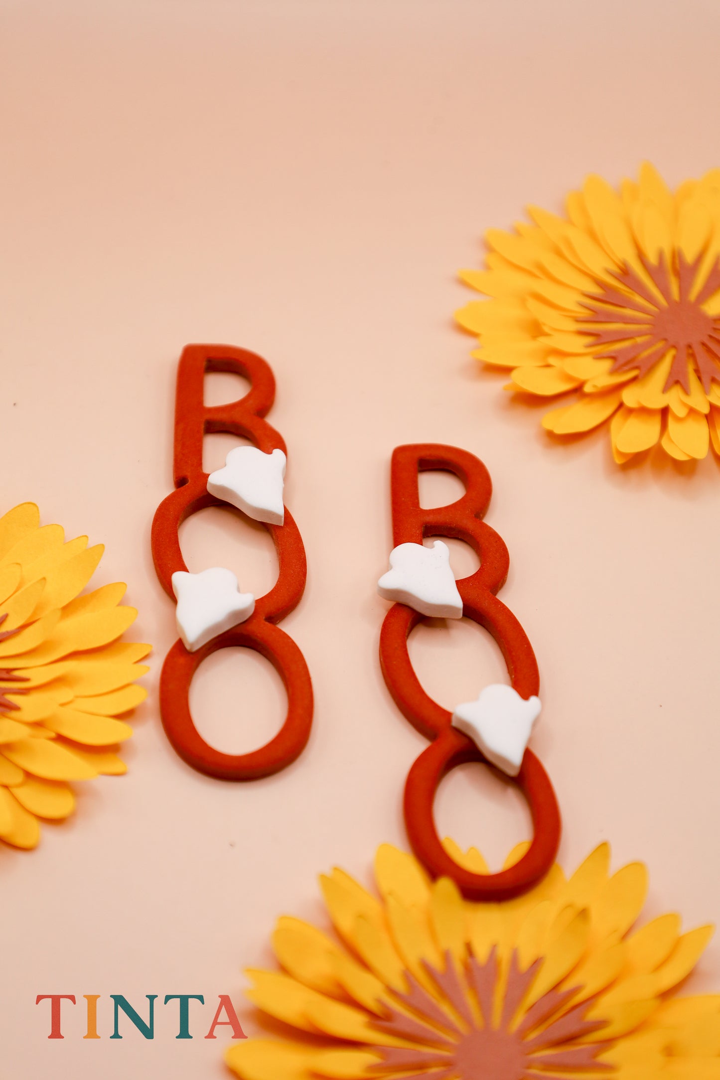 Red letter 'B' with white hearts surrounded by yellow flowers on a beige background, featuring the brand 'Tinta'.