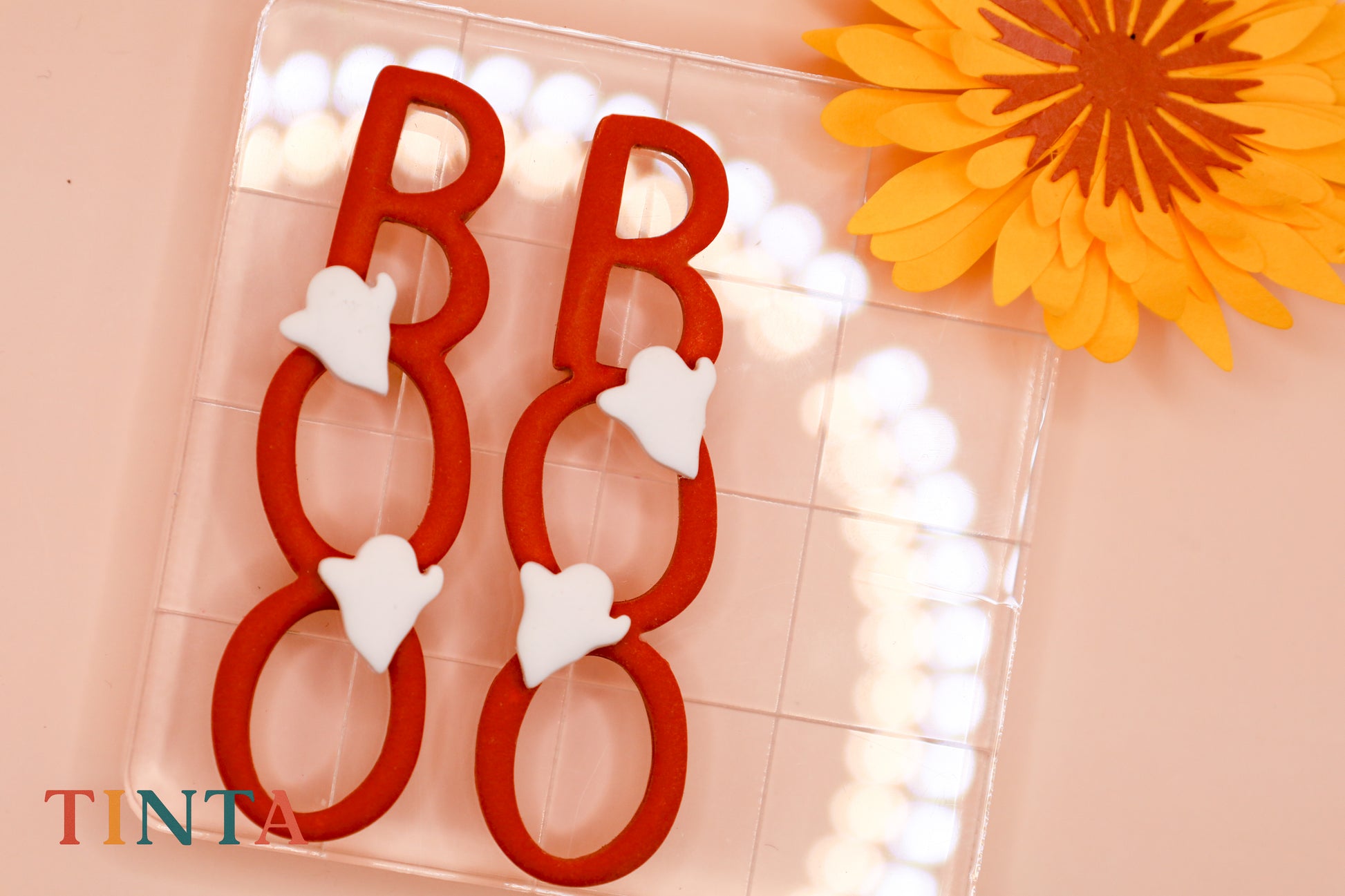 Red letter 'B' with white hearts on a pink background with a yellow flower.