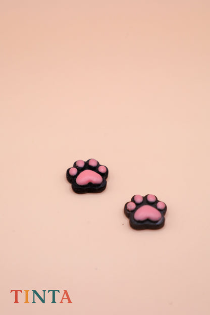Pink paw-shaped earrings on a beige background with 'TINTA' branding.