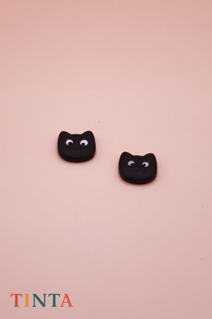Black cat-shaped earrings on a pink background with 'TINTA' branding.