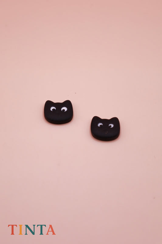 Black cat-shaped earrings on a pink background with 'TINTA' branding.