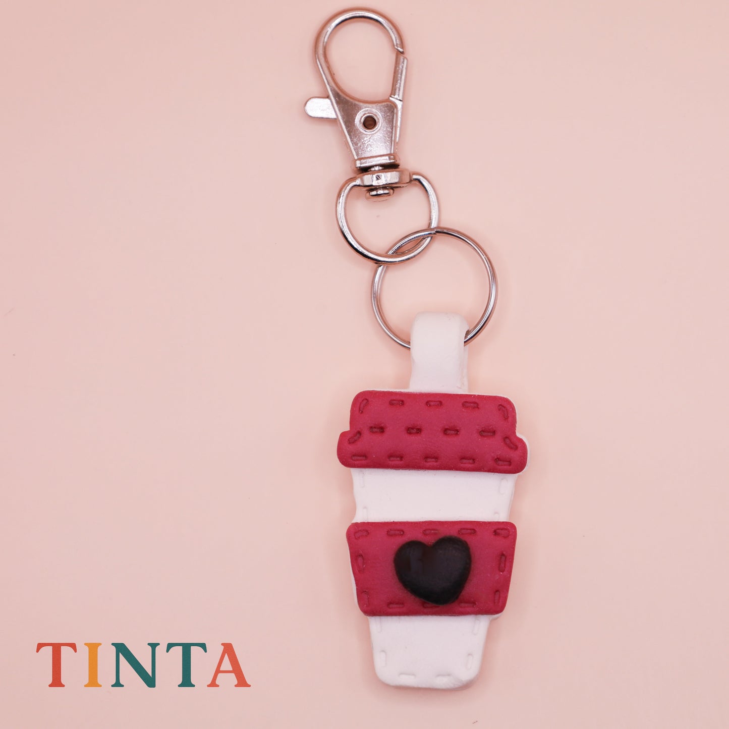 Keychain with coffee cup design on a beige background, featuring the brand 'Tinta'.