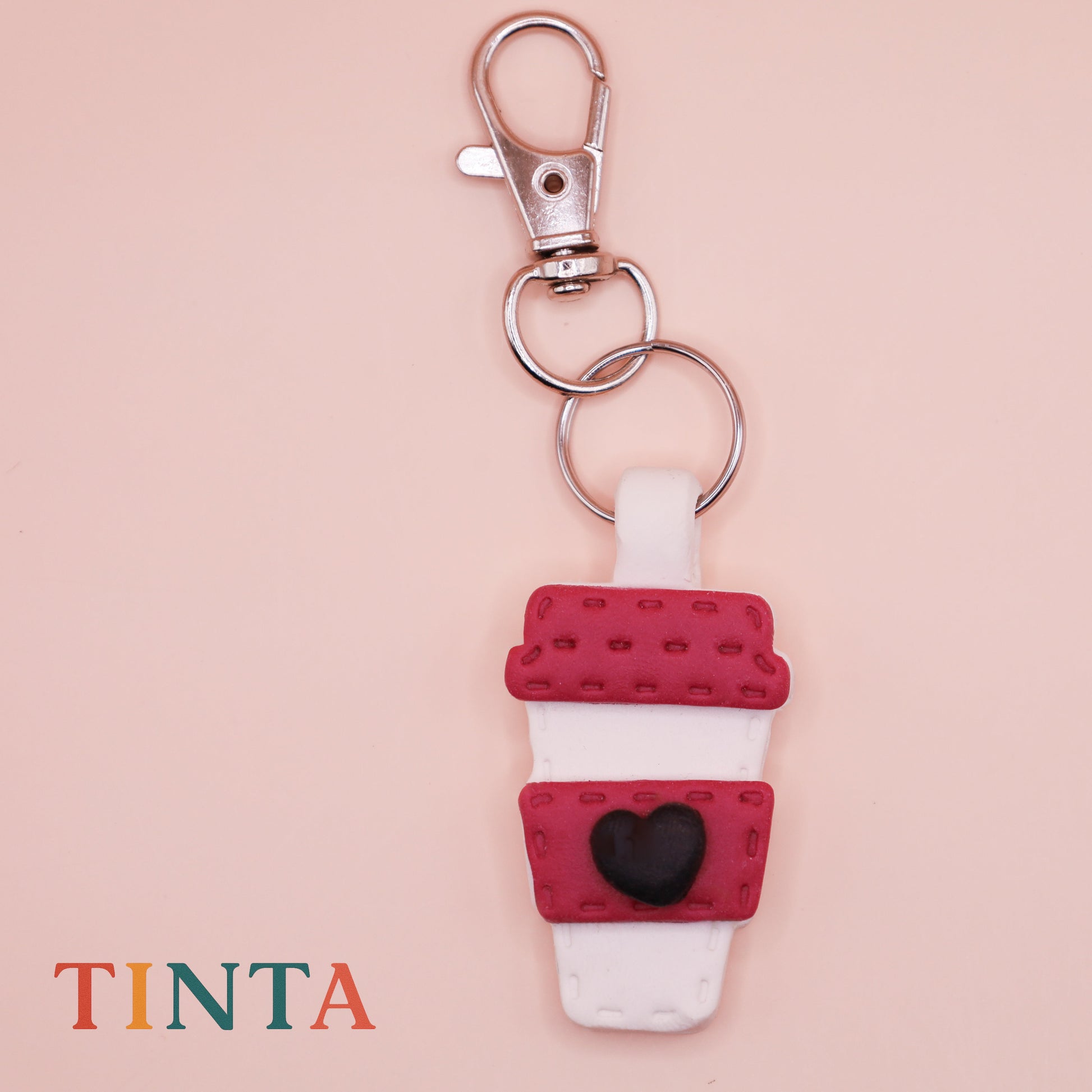 Keychain with coffee cup design on a beige background, featuring the brand 'Tinta'.