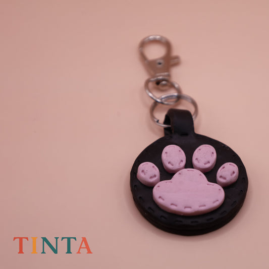 Keychain with pink paw print design on a beige background, featuring the brand 'TINTA'.
