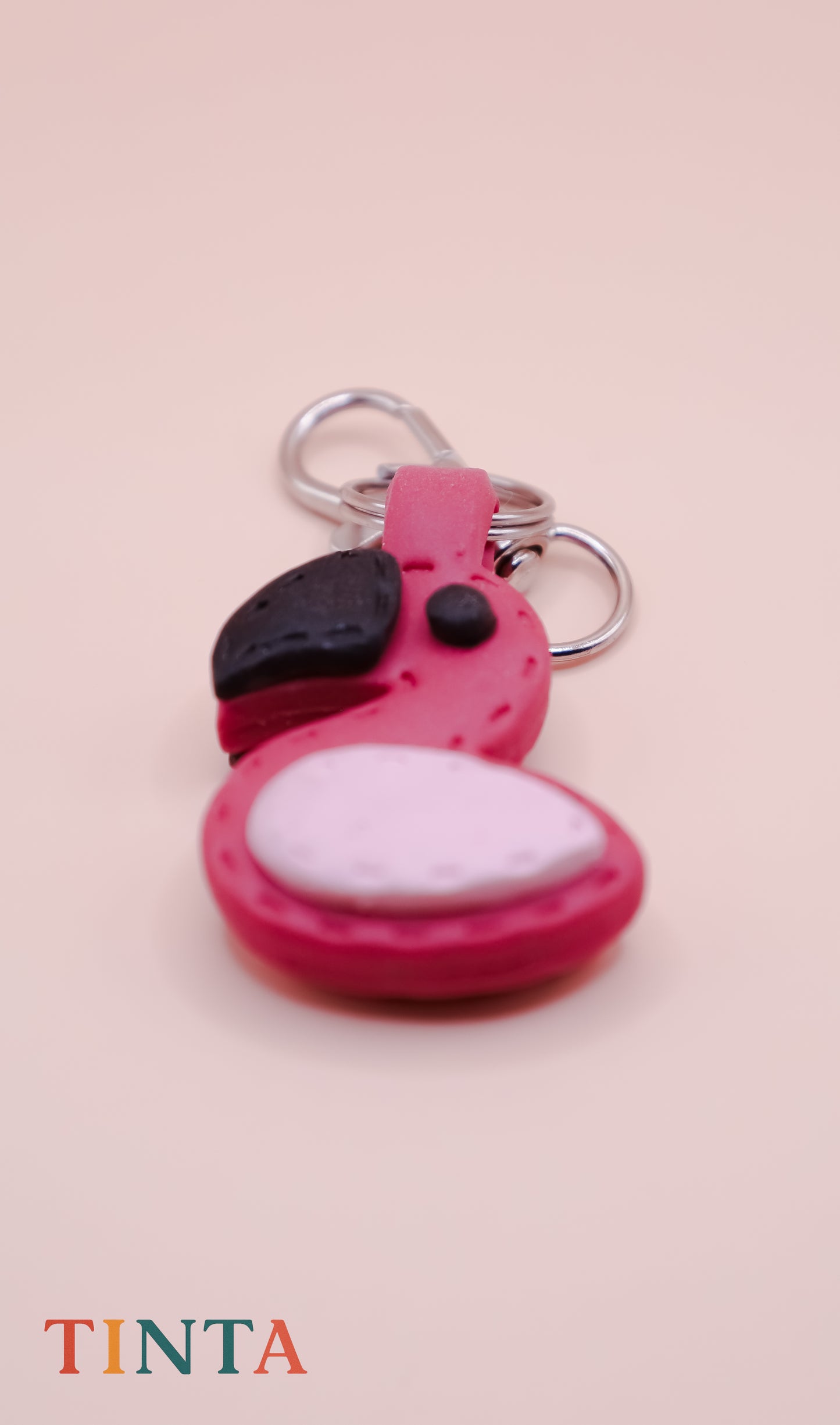 Pink flamingo keychain with black and white accents on a pink background, featuring the brand 'TINTA'.