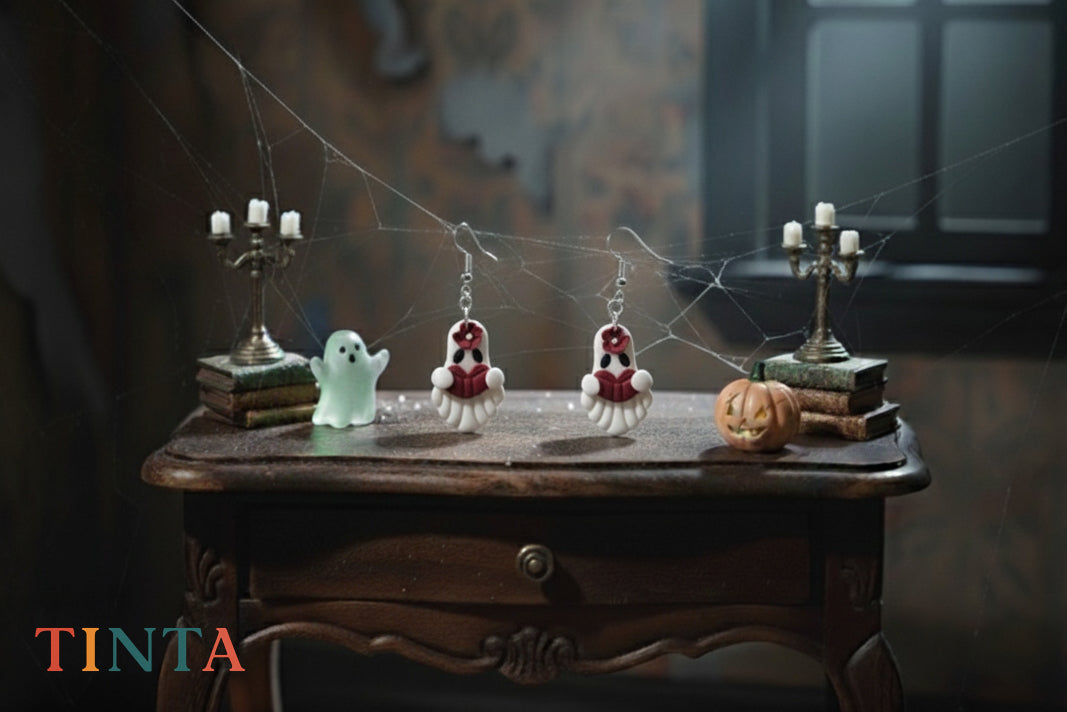 Halloween-themed earrings on a wooden table with ghost and pumpkin decorations, featuring the brand 'TINTA'.