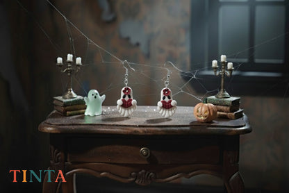 Halloween-themed earrings on a wooden table with ghost and pumpkin decorations, featuring the brand 'TINTA'.