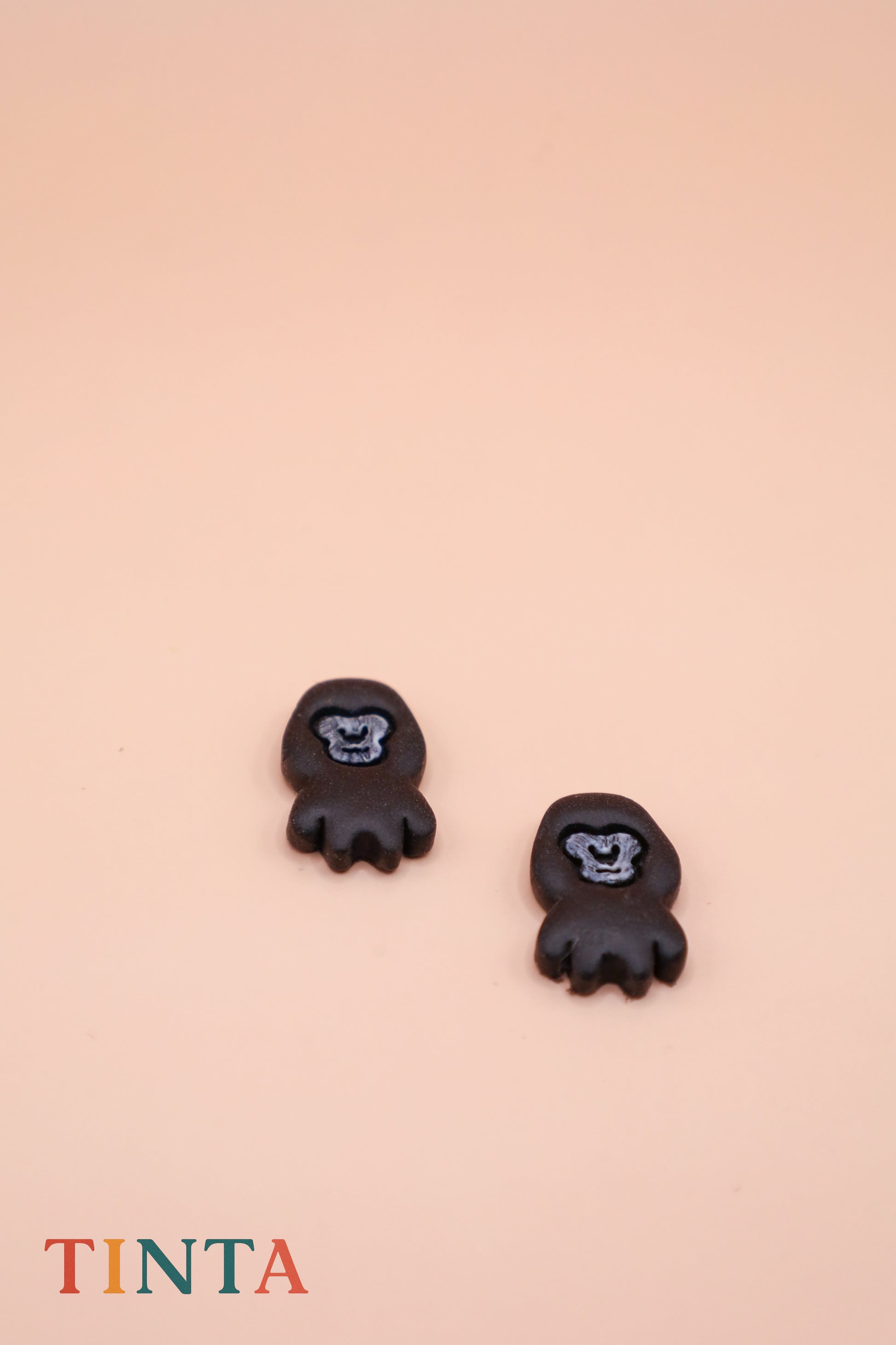 Black animal-shaped earrings on a beige background with 'TINTA' branding.
