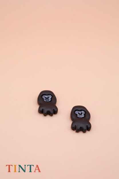 Black animal-shaped earrings on a beige background with 'TINTA' branding.