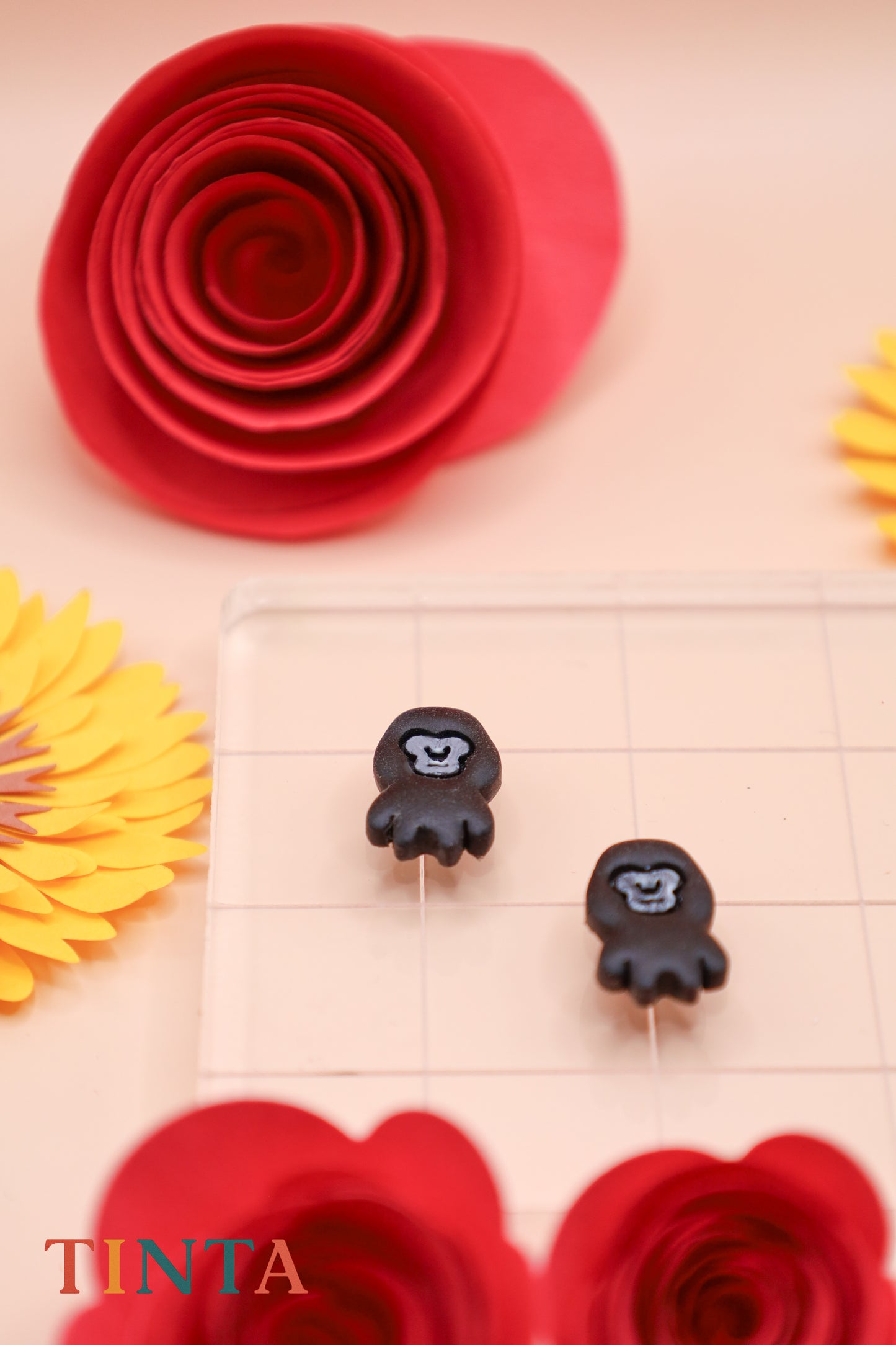 Black monkey-shaped earrings on a beige surface with red and yellow floral decorations.