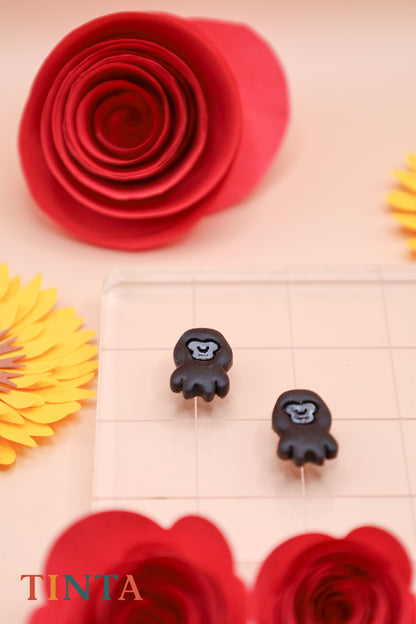 Black monkey-shaped earrings on a beige surface with red and yellow floral decorations.