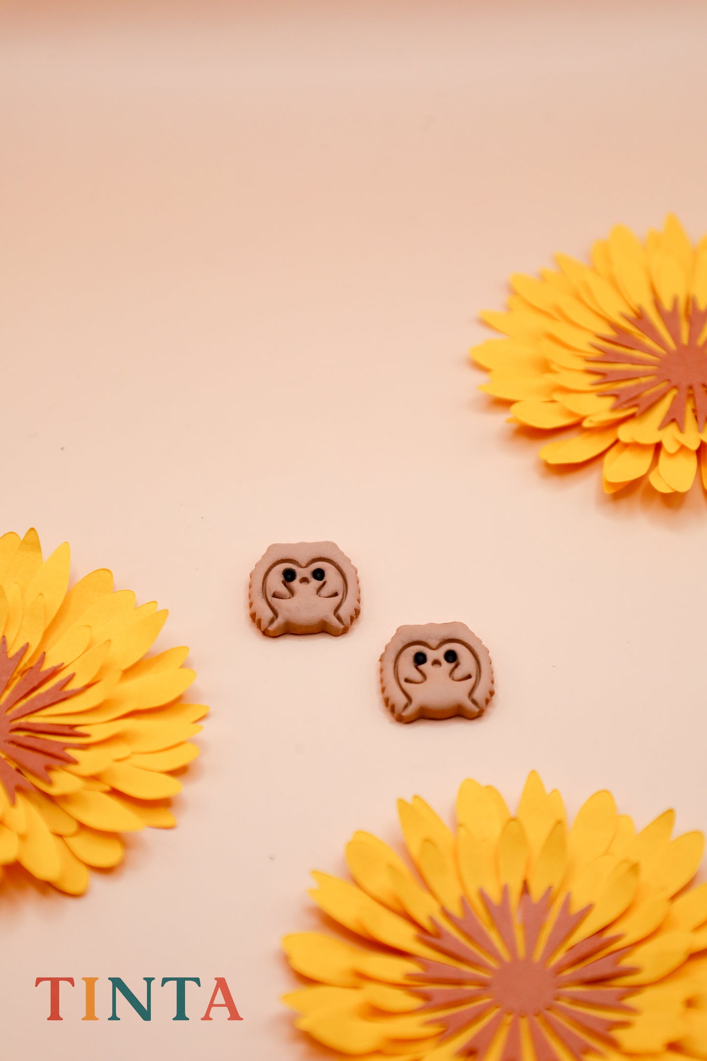 Two small animal-shaped cookies with a beige background and yellow flowers, featuring the brand 'Tinta'.