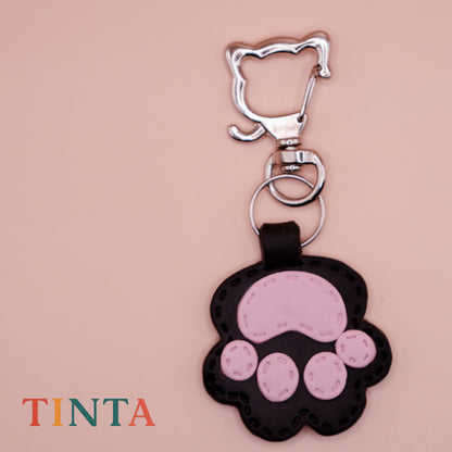 Keychain with pink paw design on a beige background, featuring the brand 'Tinta'.