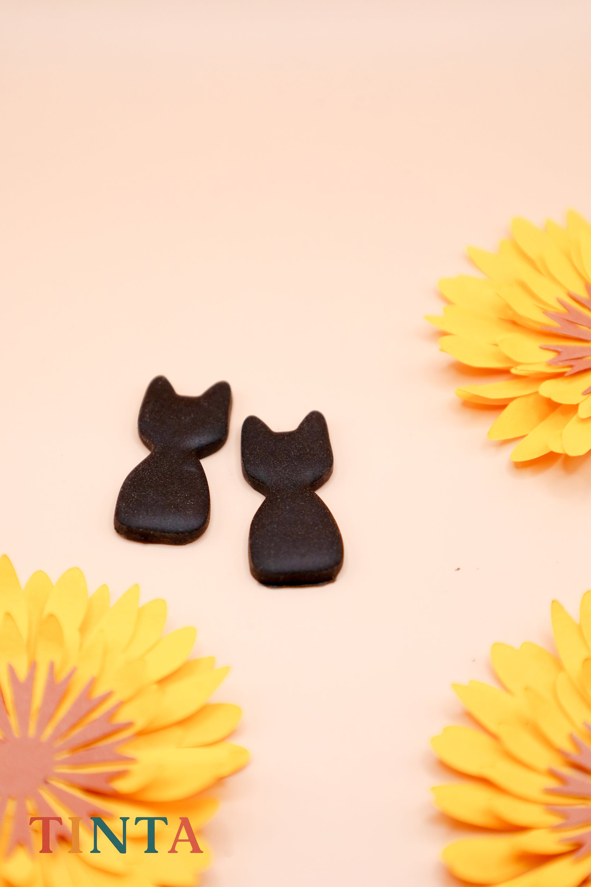 Two black cat-shaped cookies on a pink background with yellow flowers.