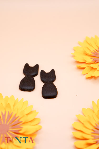 Two black cat-shaped cookies on a pink background with yellow flowers.