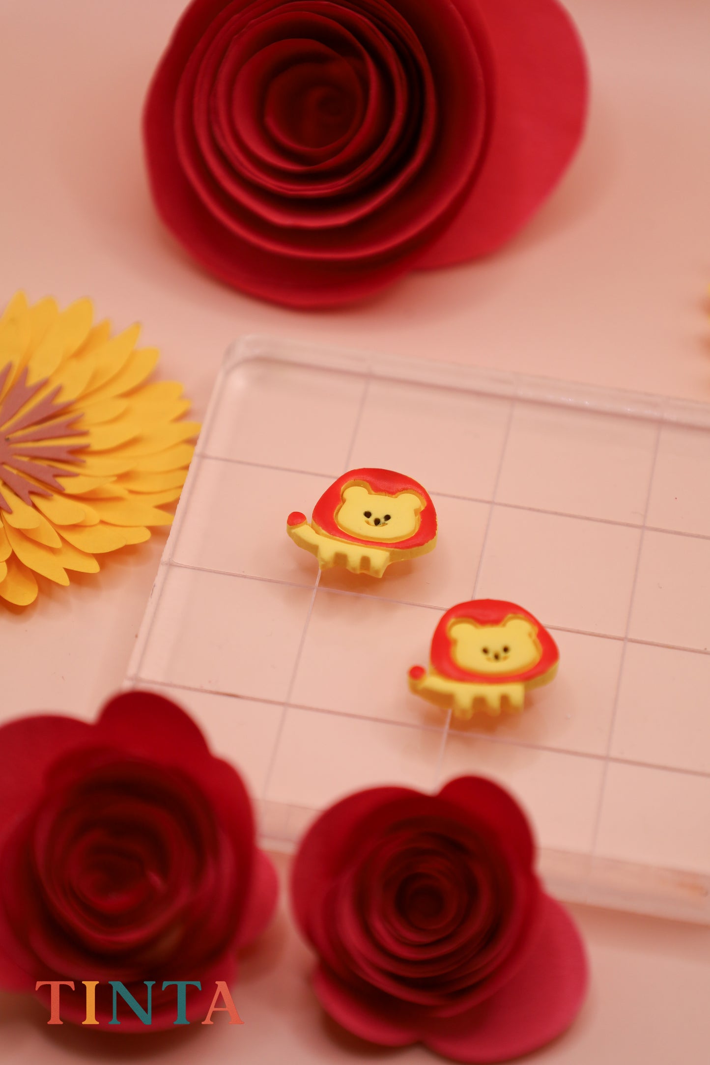 Two lion-shaped stamps on a cutting mat with red and yellow paper flowers around.
