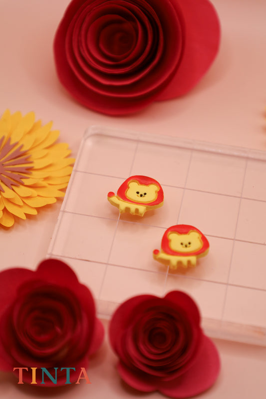 Two lion-shaped stamps on a cutting mat with red and yellow paper flowers around.