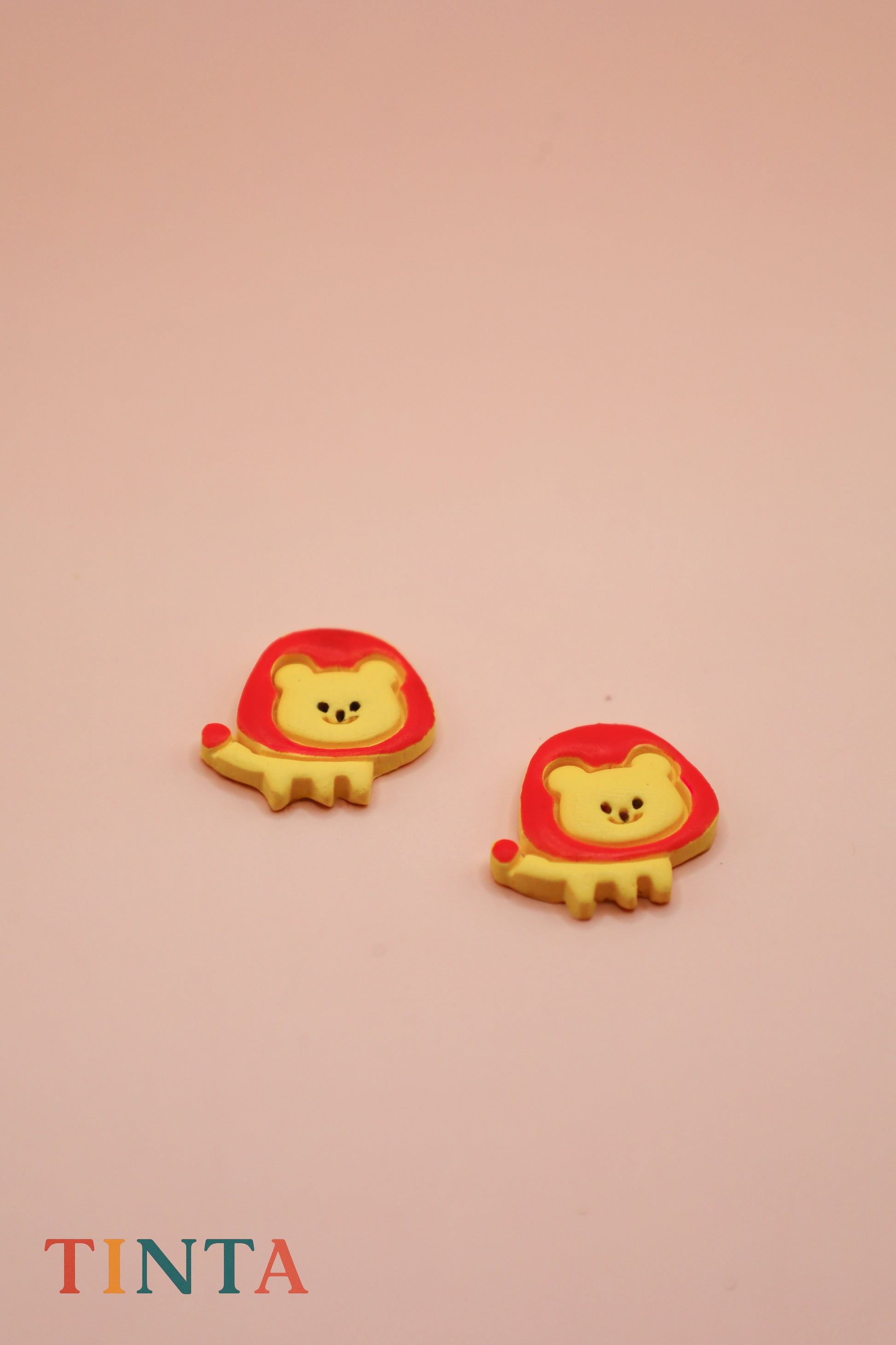 Two lion-shaped cookies with red crowns on a beige background, featuring the brand 'Tinta'.