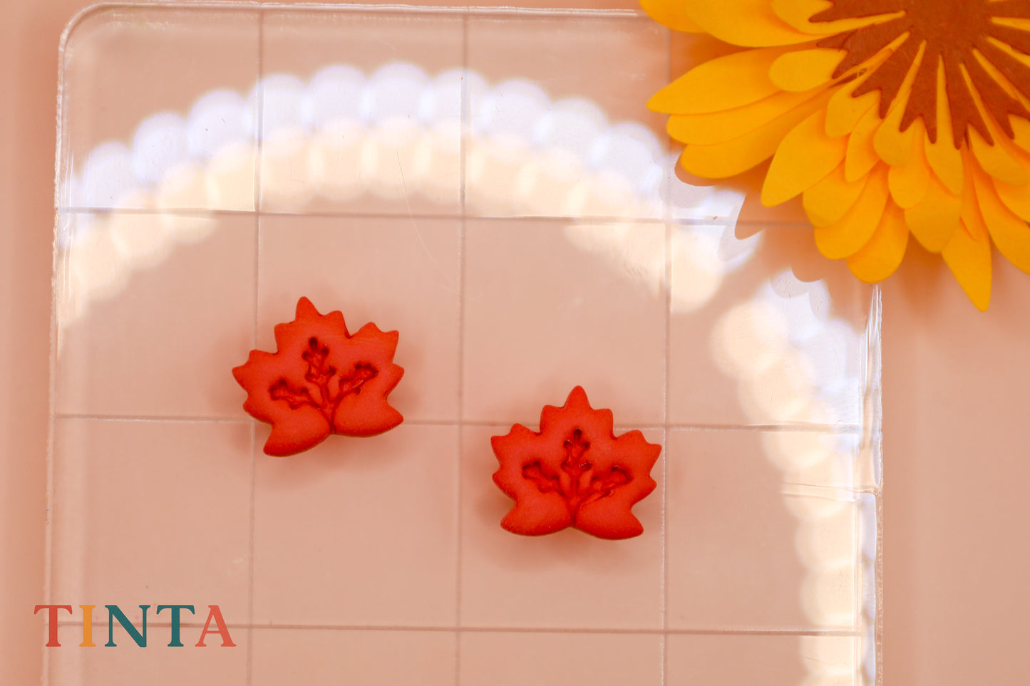 Red floral-shaped objects on a clear surface with a yellow flower in the corner, featuring the brand 'TINTA'.