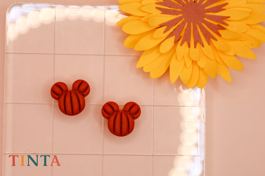 Red mouse ear earrings on a white surface with a yellow flower in the background, featuring the brand 'TINTA'.
