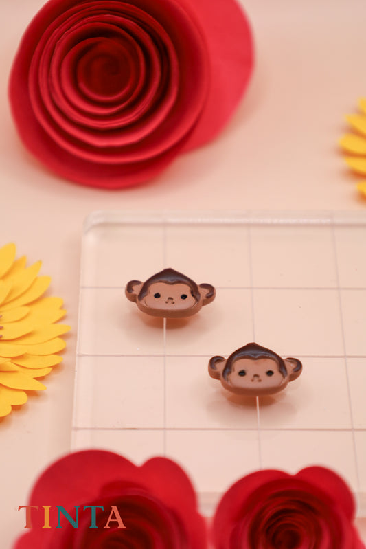 Two small monkey figurines on a grid with red and yellow flowers around.