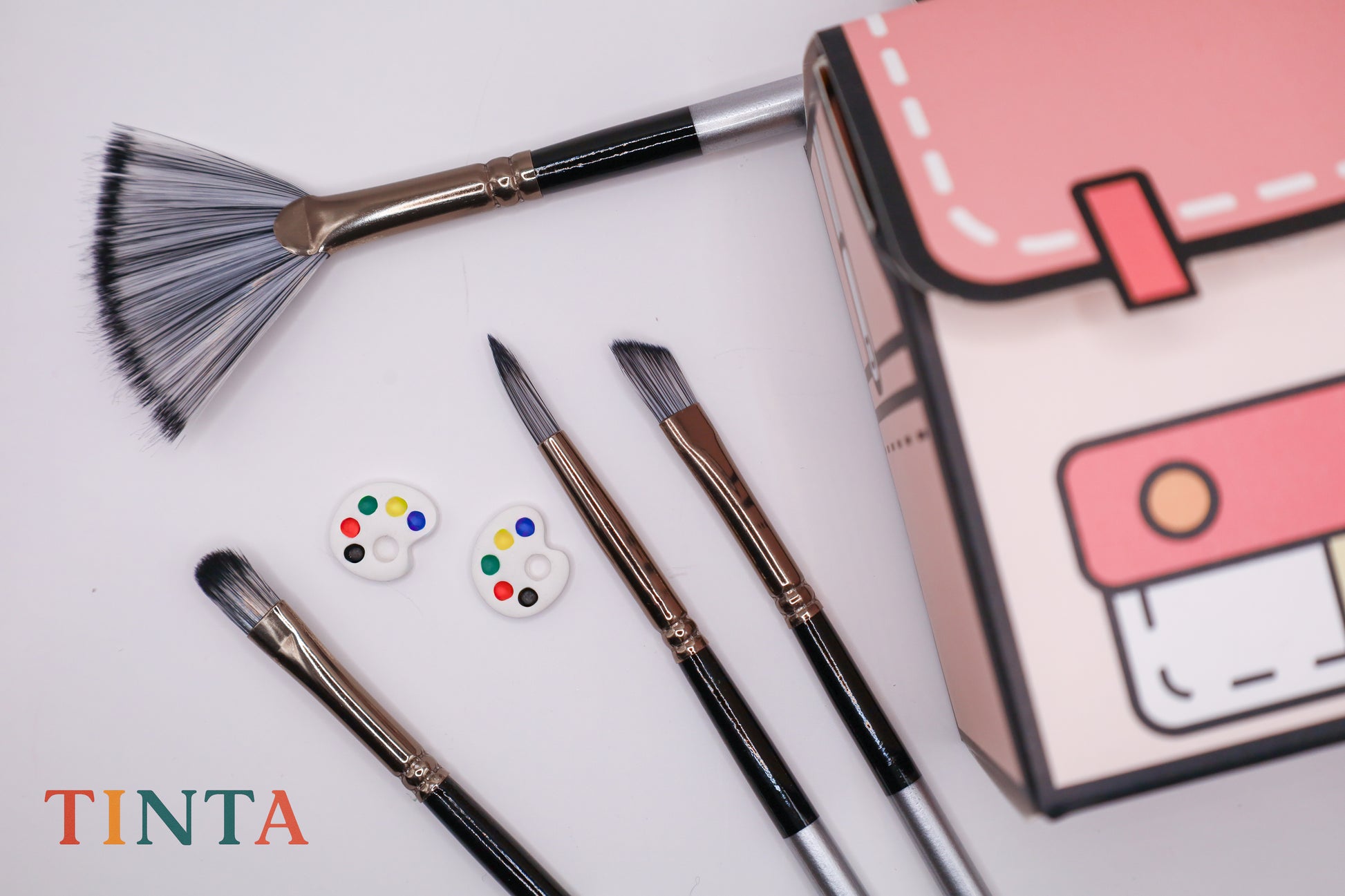Set of paintbrushes and a small pink case on a light background, with 'TINTA' branding.