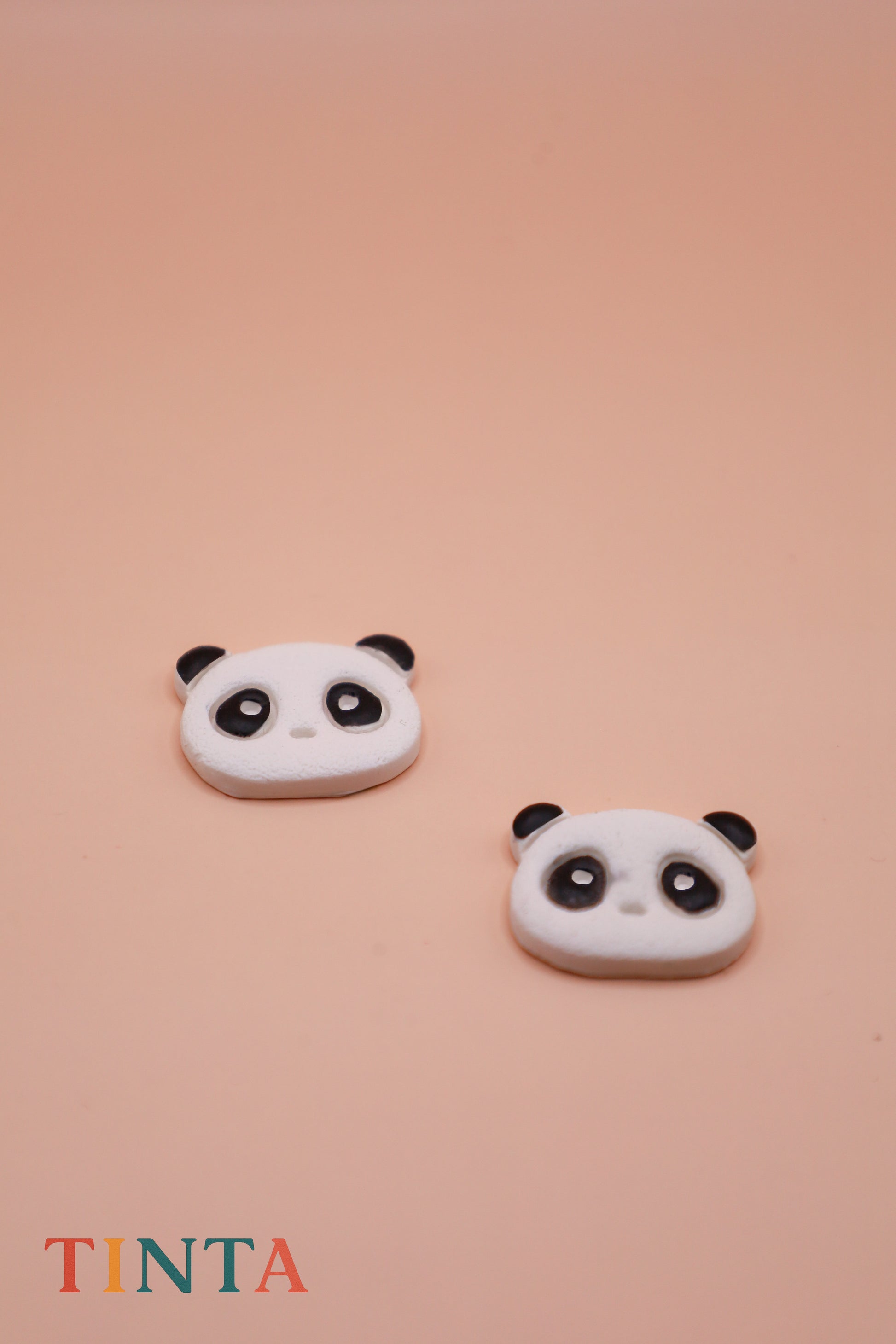 Two panda-shaped earrings on a pink background with 'TINTA' branding.