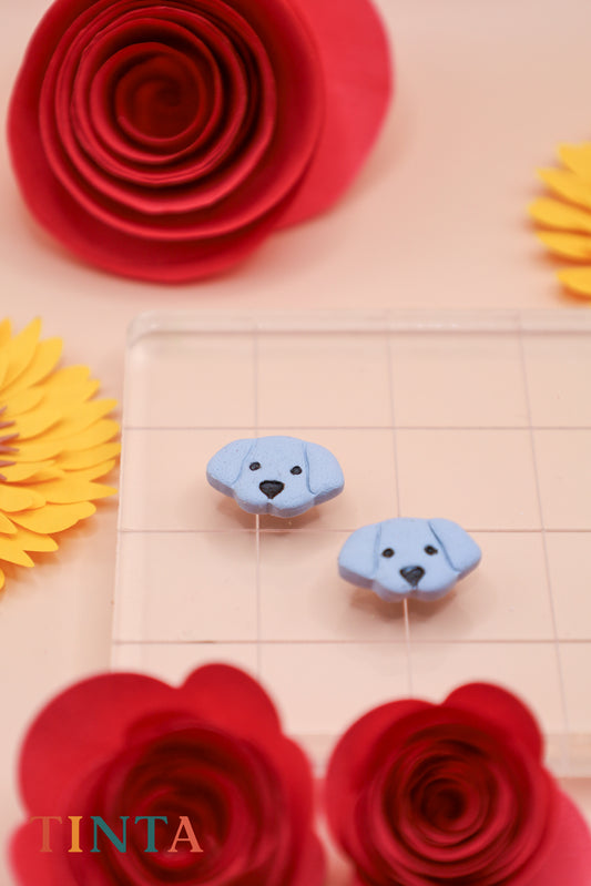 Blue dog-shaped earrings on a beige background with red and yellow flowers.