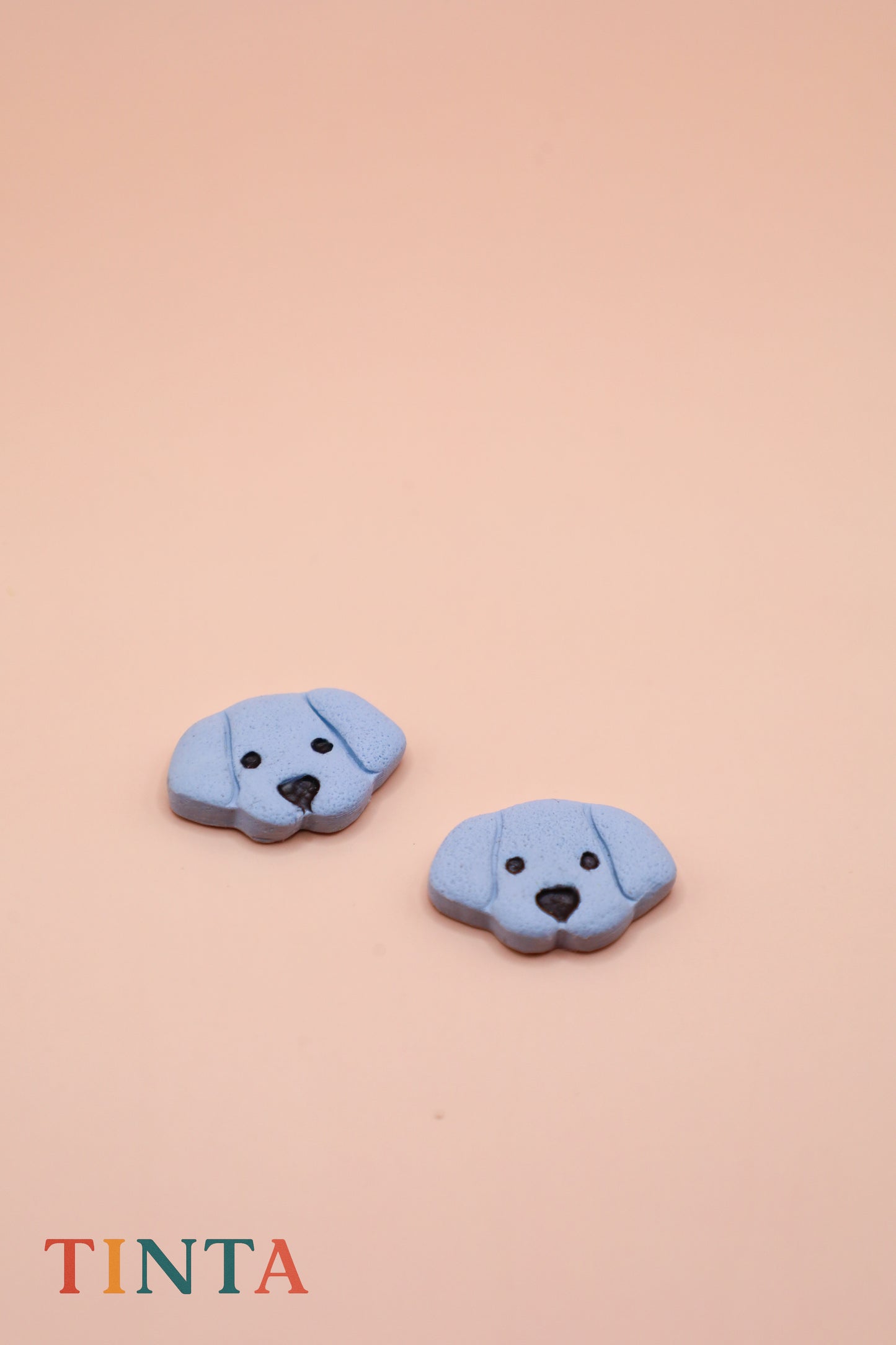 Two blue dog-shaped buttons on a beige background with 'TINTA' branding.