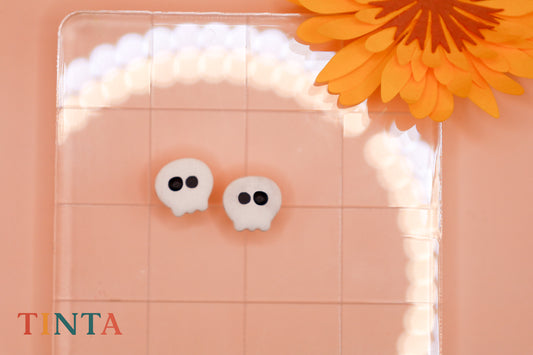 White skull-shaped earrings on a pink background with an orange flower.