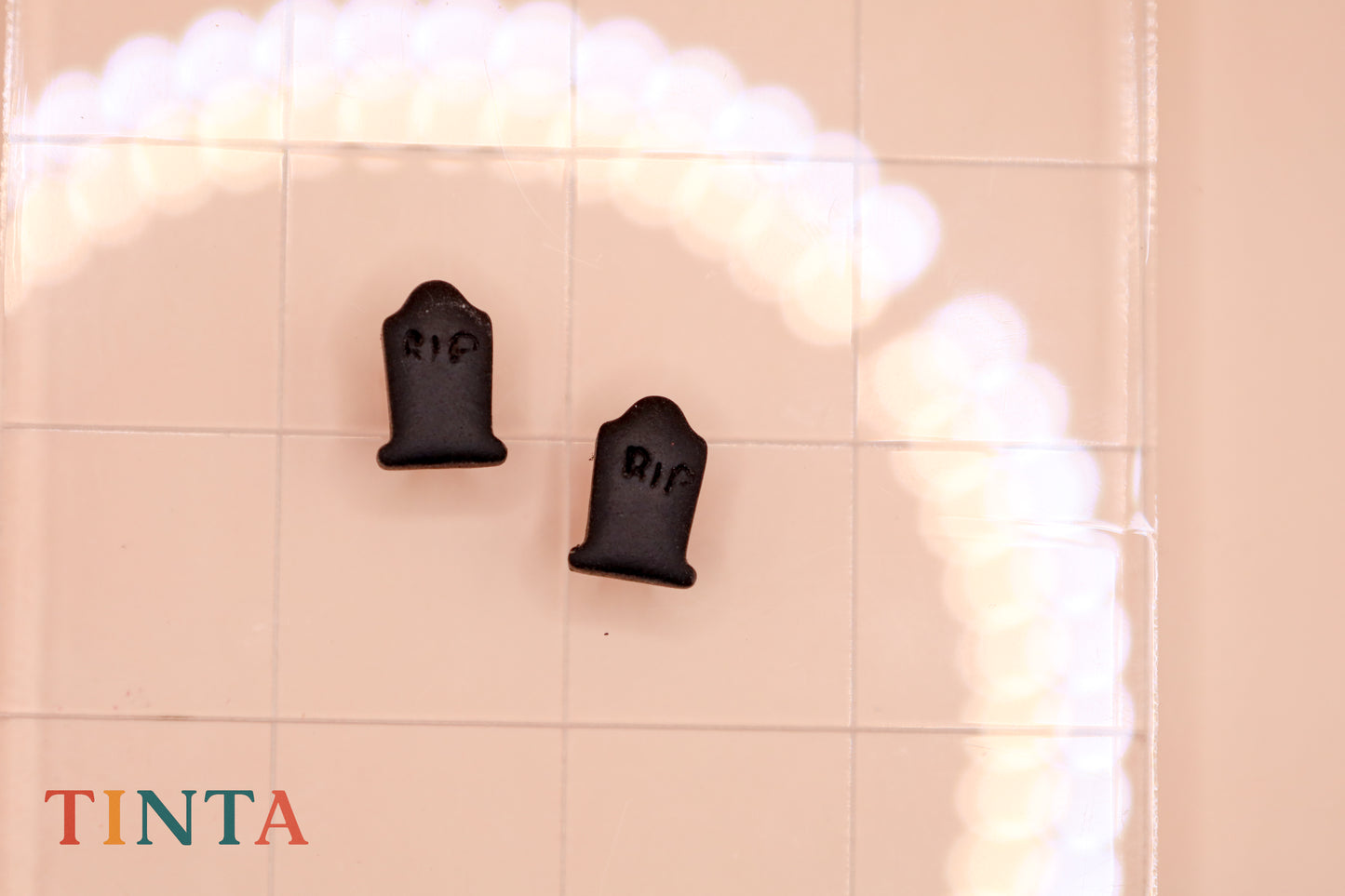 Two black tombstone-shaped objects with 'RIP' on a tiled wall, featuring the brand 'TINTA'.